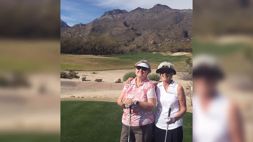 两位女士戴着帽子在山前打高尔夫球