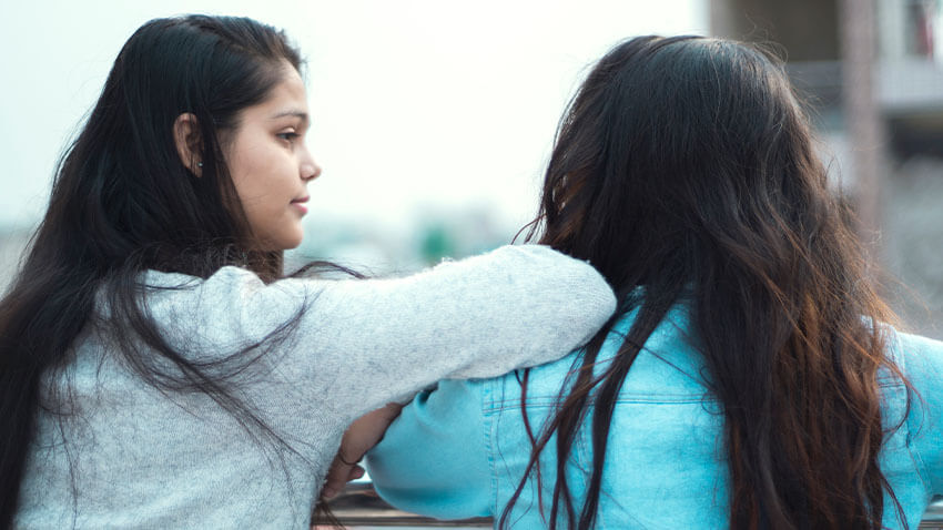 有长的黑发的女孩看和倾斜在朋友的肩膀与长的棕色头发和蓝色衬衣