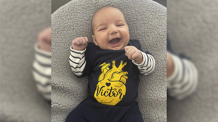 婴儿在灰色枕头上微笑，穿着蓝黄衬衫和条纹内袖衬衫