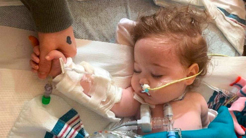 Baby sleeping in hospital bed with tubes holding moms hand