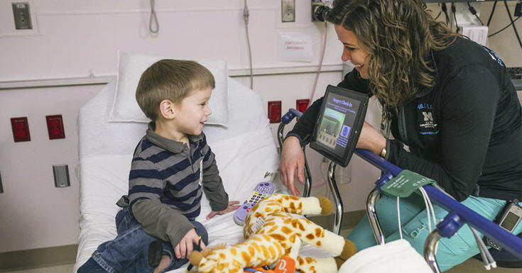 有长颈鹿玩具的孩子在医院病床与童心专用锡黑衬衣坐在床上