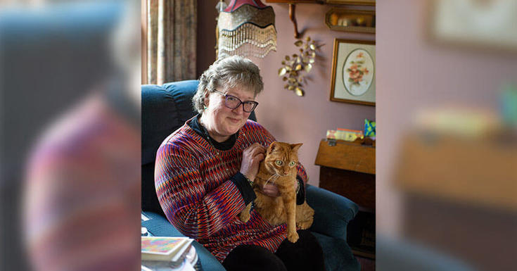 女人坐在扶手椅上，抱着一只橙色的猫