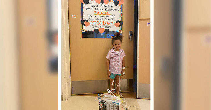 一个小女孩站在医院门口，她身后的牌子上写着“这应该是我上幼儿园的第一天。”