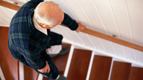 一名年长男子在走下木楼梯时弯腰扶着栏杆